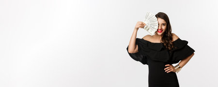 Beauty and shopping concept. Fashionable woman with red lips, showing dollars and smiling, standing over white background with moneyの写真素材