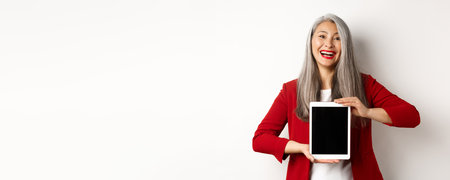 Business. Cheerful asian businesswoman in red blazer, showing digital tablet screen and smiling, introduce app or promotion, white backgroundの写真素材