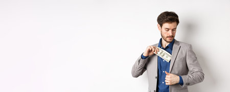 Successful businessman put dollars inside suit pocket, hiding money, standing on white backgroundの写真素材