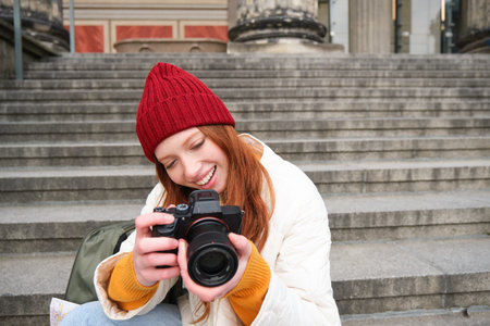 Portrait of young photographer girl, sits on stairs with professional camera, takes photos outdoors,...