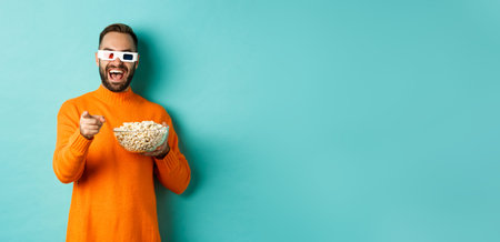 Man watching comedy in 3d glasses, eating popcorn, laughing and pointing at camera tv screen,...