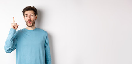 Image of excited handsome man pitching an idea, raising finger and saying eureka, standing over white backgroundの写真素材