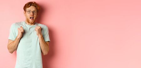 Portrait of scared redhead guy in glasses staring startled at camera, press hands to body and scream of fear, standing over pink backgroundの写真素材