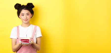 Asian birthday girl standing with cake and smiling, celebrating b-day on yellow backgroundの写真素材