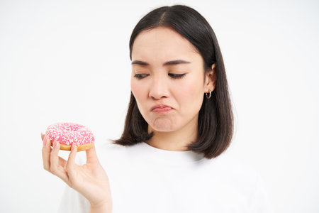 Close up of sad cute girl, shows tasty glazed doughnut, being on diet, cant try delicious donnut, junk food conceptの写真素材