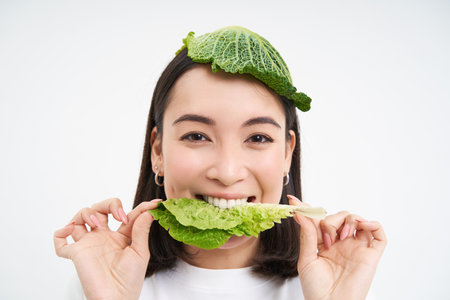 Portrait of cute smiling korean woman with leaf on head, eats cabbage and looks happy, white backgroundの写真素材