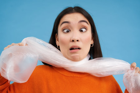 Close up portrait of korean woman being choked by large plastic bag, concept of sustainable...