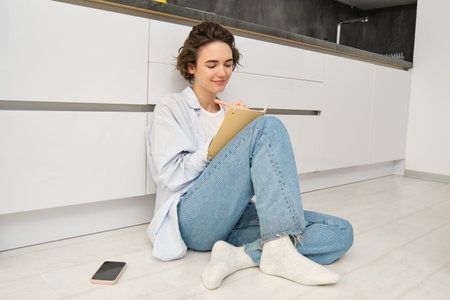 Portrait of creative young woman, artist sits on floor and draws in her planner, writes diary,...