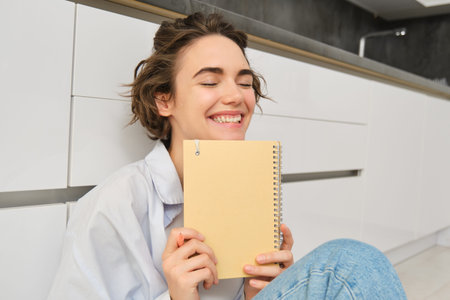Portrait of happy, carefree woman, writes in her journal and laughs, holds her diary, reads...