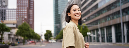 Outdoor shot of asian girl with laptop, going somewhere in city centre, walking on street, going to workの写真素材