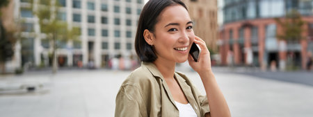 Cellular connection. Young asian woman makes a telephone call, talking on mobile smartphone and walking on streetの写真素材