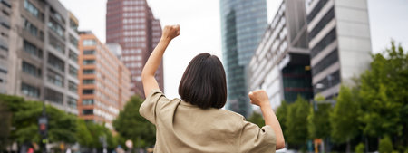 Excitement. Happy girl rear view, raising her hands up and looking at big city skyscrappers, feeling...