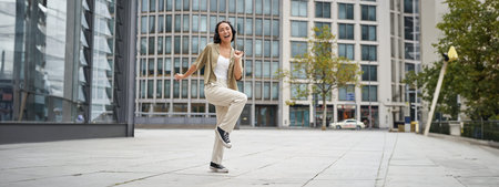 Happy people in city. Upbeat young girl dancing on street in headphones, listening music in...