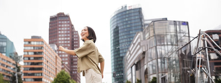 Vertical shot of young asian woman posing happy, raising hands up and dancing, triumphing,...