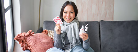 Portrait of happy smiling asian girl showing medication, sore throat spray and drugs from flu or...