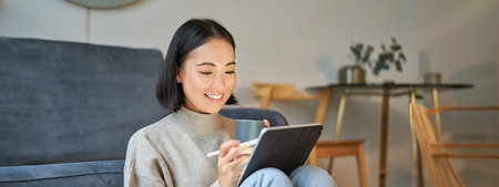 Smiling korean woman sitting with tablet and pen, drawing and scatching her new project or design,...