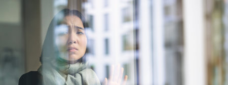 Asian woman feels unwell, stays at home, looks outside window with jealous, distressed face, wants...