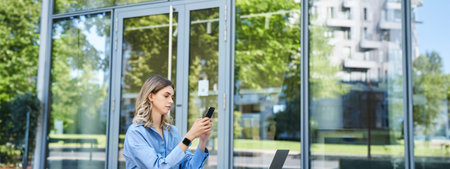 Portrait of businesswoman sitting outdoors and working. Young corporate woman looking at her...