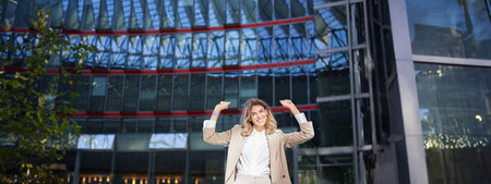 Happy businesswoman dancing on street, raising hands up. Corporate woman celebrates her victory or successの写真素材