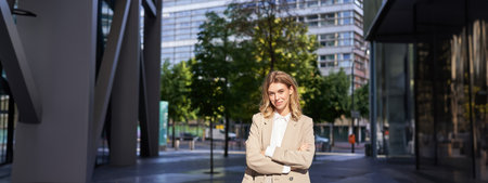 Portrait of smiling businesswoman in corporate clothing, looking confident and happy, wearing beige suit, standing outdoors on street, outside officeの写真素材