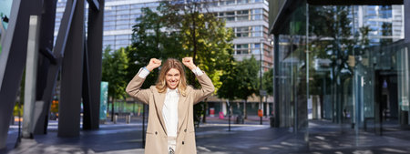 Portrait of successful business woman, young corporate woman celebrating victory, achievement, triumphing on street, making fist pumps and rejoicingの写真素材
