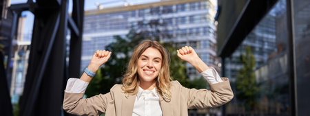 Happy smiling saleswoman in beige suit, celebrates her achievement, triumphing, making fist pump and...