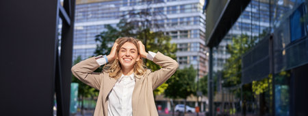Excited businesswoman, office lady in suit, rejoicing, standing on street and celebrating, feeling happy, posing outdoors near office buildingsの写真素材