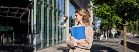 Portrait of businesswoman in beige suit and high heels walking on street. Corporate woman going to...