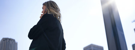 Portrait of stylish corporate woman talking on mobile phone, having a call while walking on street,...