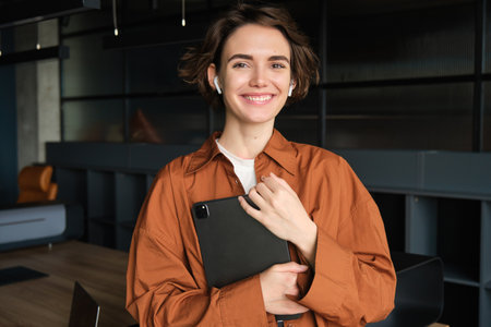 Portrait of young female employee, social media content creator working in office, holding digital tablet, smiling and looking happyの写真素材