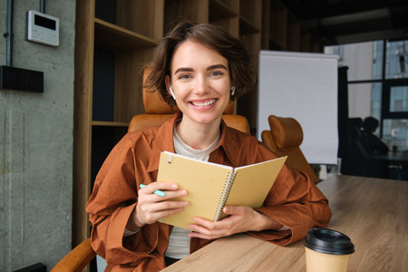 Portrait of business woman in casual clothes, working in office, holding her notebook, writing down, making notes during a meeting, brainstormingの写真素材