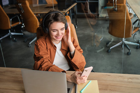 Image of digital nomad, woman working in office, sitting with laptop and wireless headphones,...