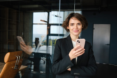 Image of corporate woman, saleswoman in business company, standing in black suit, holding...