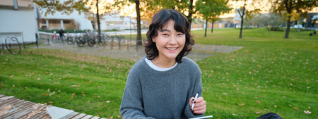 Portrait of young smiling korean girl, graphic designer, artist drawing on digital tablet with a pen tool, sitting in park on fresh air and scatching, taking notesの写真素材