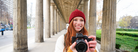 Smiling tourist photographer, takes picture during her trip, holds professional camera and makes photosの写真素材