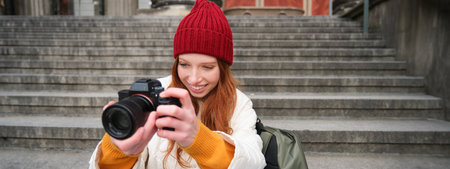 Portrait of young photographer girl, sits on stairs with professional camera, takes photos outdoors, making lifestyle shootingの写真素材
