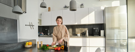 Portrait of good-looking woman cooking salad in the kitchen, chopping vegetables and smiling, preparing healthy meal, leading healthy lifestyle and eating raw foodの写真素材