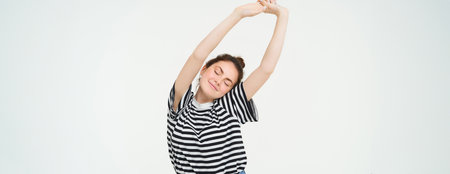 Image of beautiful girl stretching her arms with pleased, satisfied face expression, isolated against white backgroundの写真素材