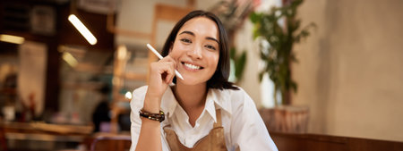 Close up portrait of smiling brunette asian woman, sitting with graphic pen and looking happy,...