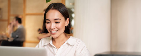 Stylish brunette woman with laptop, sitting in cafe and drinking coffee, smiling happily