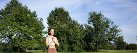 Young mindful woman, meditating on fresh air, doing yoga exercises in park, standing on rubber mat in sportswearの写真素材