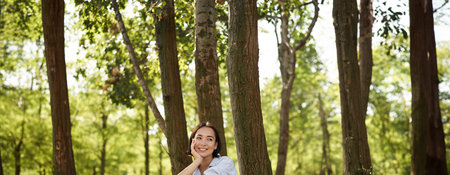 Woman sitting in park with her favourite book, leaning on tree under shade on sunny day, enjoying...
