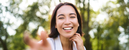 Genuine people. Portrait of asian woman laughing and smiling, walking in park, feeling joy and positivityの写真素材