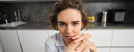 Close up portrait of young woman, 25 years old, sitting in her kitchen alone, express candid...