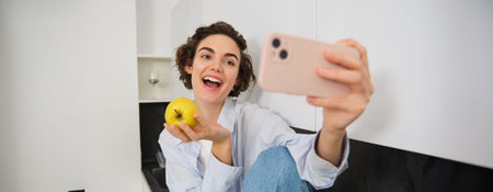 Beautiful woman eating an apple and recording herself on video. Cute girl with fruit, posing for...