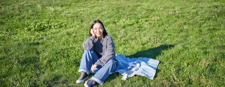 Young asian girl enjoying sunny day outdoors. Happy student having picnic on grass in park, playing...