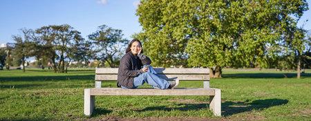 Portrait of young asian woman sitting on bench with smartphone. Cute girl using mobile phone,...