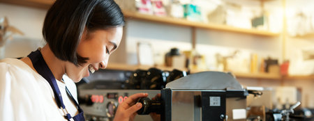 Happy asian woman, barista using coffee machine to make order, steaming milk for cappuccino and...