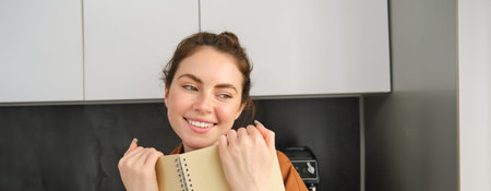 Close up portrait of cute girlfriend, giggle, reading notebook, holding planner and smiling at...