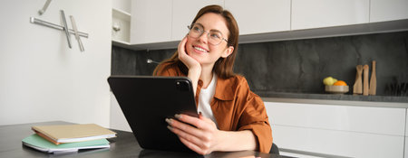 Portrait of young student, woman studying at home, working remotely, setup workplace in her kitchen,...